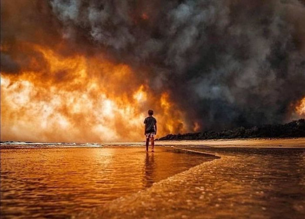 A boy, having fled his home, watches a bushfire burn. Photo credit: Martin von Stoll.