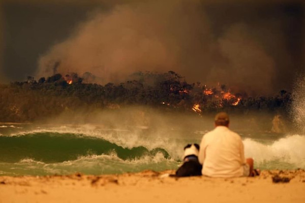 Man and dog watch a bushfire in Australia literally burn their world. Photo credit: Alex Coppel.